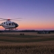 AI-generated illustration of a white and red medical helicopter flying over harvested farmland at dusk.